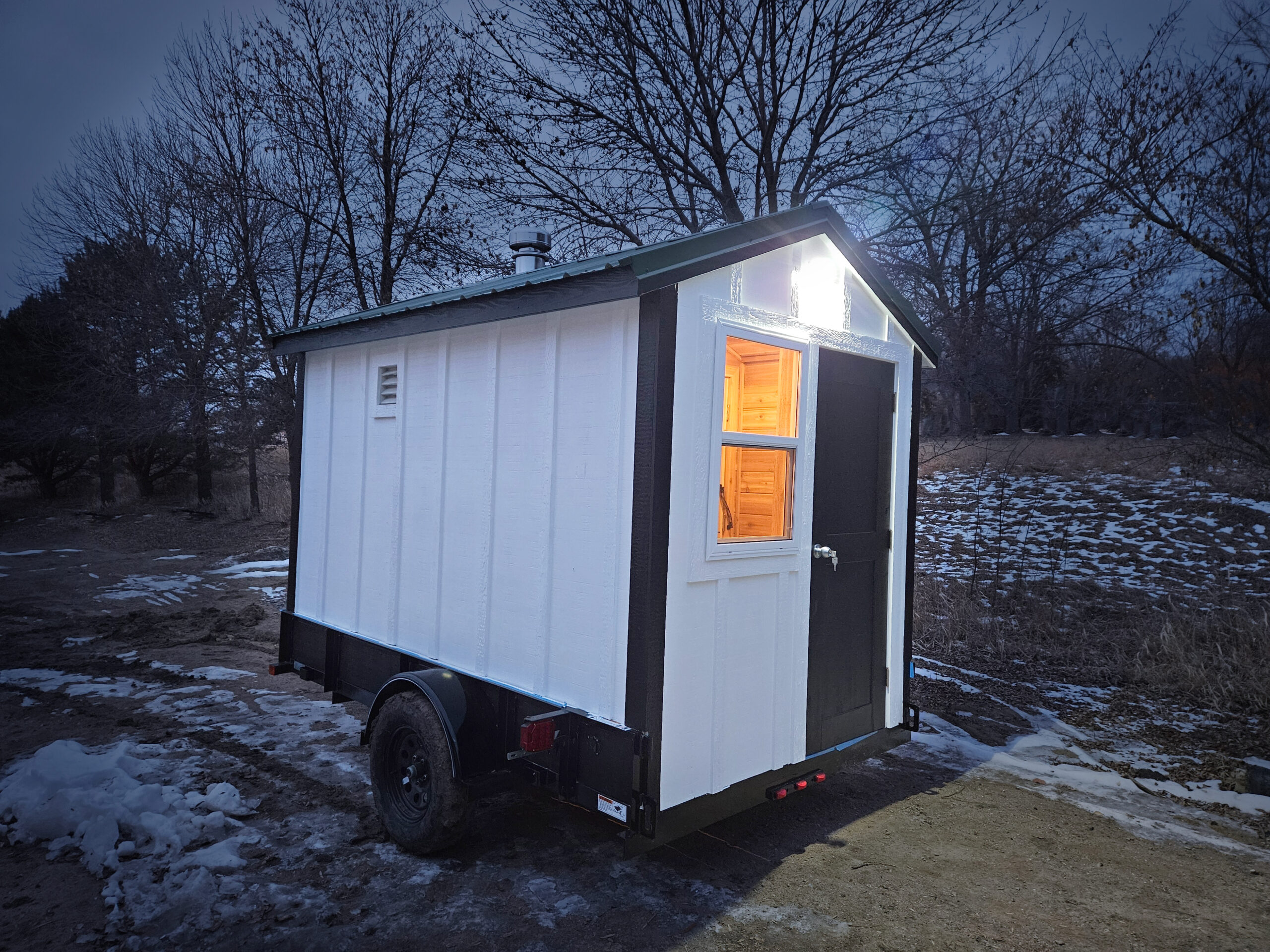 Mobile sauna at dusk with interior and exterior lights on.