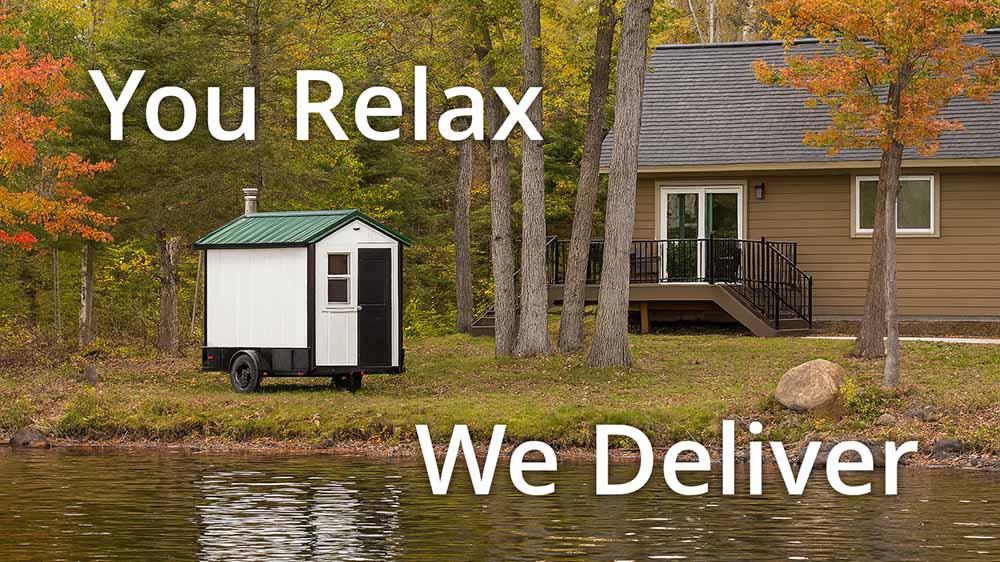 A white and black mobile sauna on a trailer parked at the edge of a lake in front of a modern cabin. The image features the text "You Relax" at the top and "We Deliver" at the bottom. The setting shows autumn trees reflecting in the water.